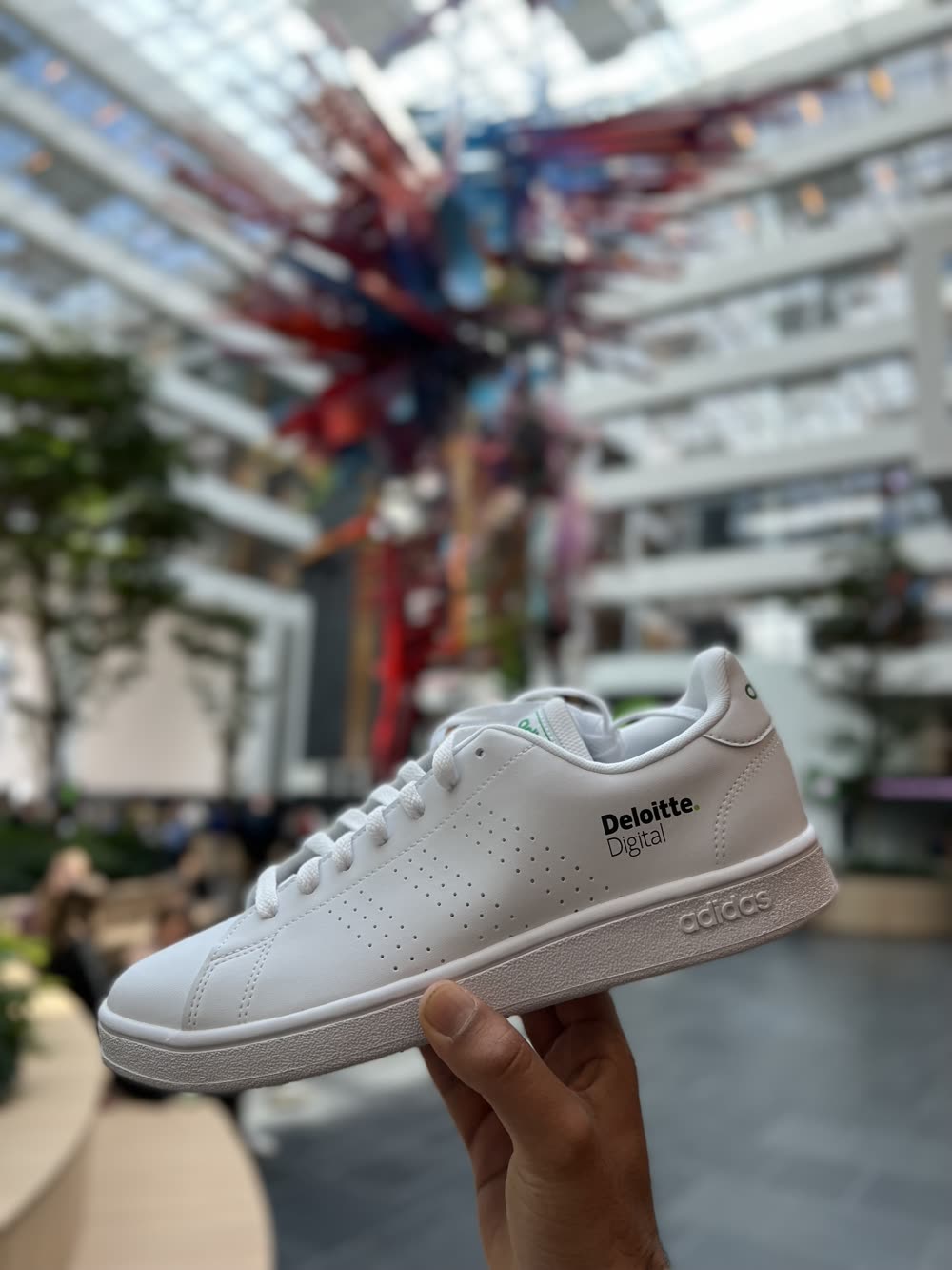 A white Adidas sneaker branded with the Deloitte Digital logo
